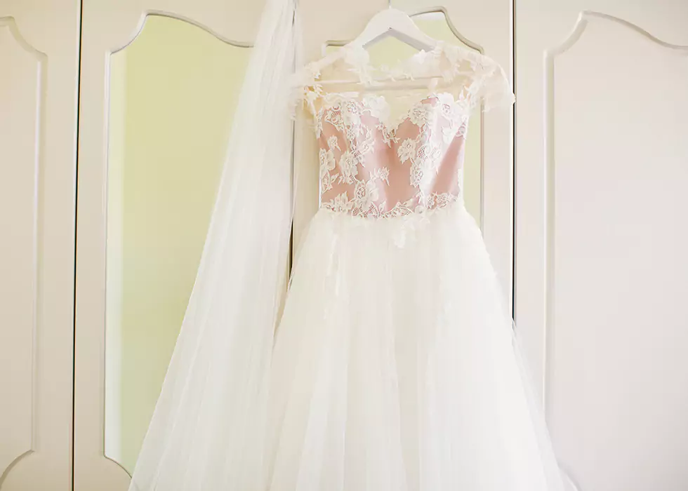 Langes weißes gesticktes Brautkleid aufgehängt an einem Kleiderbügel an einem Schrank